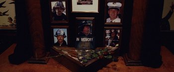 Movie still from “25th Hour” (2002), directed by Spike Lee – A table topped with flowers and a plaque with a picture of a fire fighter on it; Close Up shot, High angle