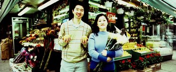 Movie still from “25th Hour” (2002), directed by Spike Lee – A man and a woman standing next to each other holding flowers; Medium shot, High angle