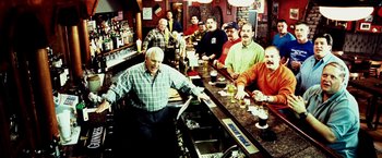 Movie still from “25th Hour” (2002), directed by Spike Lee – A group of men standing at a bar with beers; Wide shot, High angle