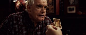 Movie still from “25th Hour” (2002), directed by Spike Lee – An older man holding a picture of himself in front of another man; Close Up shot, Over the shoulder angle