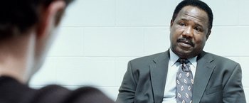 Movie still from “25th Hour” (2002), directed by Spike Lee – A man in a suit sitting in front of a brick wall; Close Up shot, Over the shoulder angle