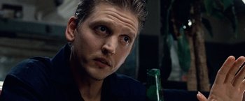 Movie still from “25th Hour” (2002), directed by Spike Lee – A person sitting at a table with a bottle; Close Up shot, Over the shoulder angle