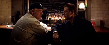 Movie still from “25th Hour” (2002), directed by Spike Lee – Two men sitting at a table in front of a fireplace; Medium shot, Over the shoulder angle