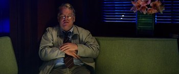 Movie still from “25th Hour” (2002), directed by Spike Lee – A man sitting on top of a green couch wearing glasses; Medium shot, High angle