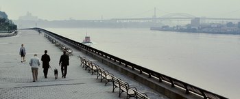 Movie still from “25th Hour” (2002), directed by Spike Lee – A row of benches on the side of a river with a boat in the background; Extreme Wide shot, High angle