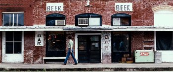 Movie still from “25th Hour” (2002), directed by Spike Lee – A man walking down the sidewalk in front of a bar; Extreme Wide shot, High angle
