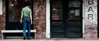 Movie still from “25th Hour” (2002), directed by Spike Lee – A man standing in front of a brick building with a help wanted sign on the door; Wide shot, Low angle