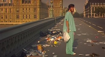 Movie still from “28 Days Later” (2002), directed by Danny Boyle – A man standing on the side of a road holding a bag; Wide shot, Low angle