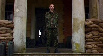 Movie still from “28 Days Later” (2002), directed by Danny Boyle – A man in a military uniform standing in front of a building; Wide shot, Low angle