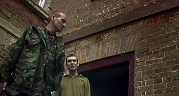 Movie still from “28 Days Later” (2002), directed by Danny Boyle – Two young men standing next to each other in front of a brick building; Medium shot, Low angle