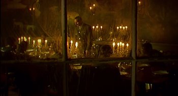 Movie still from “28 Days Later” (2002), directed by Danny Boyle – A man standing in front of a bunch of lit candles; Wide shot, High angle