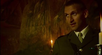 Movie still from “28 Days Later” (2002), directed by Danny Boyle – A man standing in front of a painting holding a candle; Close Up shot, Low angle