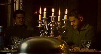 Movie still from “28 Days Later” (2002), directed by Danny Boyle – Two men sitting at a dinner table with a lit candelabrum; Medium shot, High angle