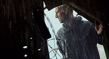 Movie still from “28 Days Later” (2002), directed by Danny Boyle – A man standing in the pouring rain looking into the distance; Medium shot, Low angle