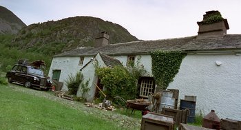 Movie still from “28 Days Later” (2002), directed by Danny Boyle – An old white house with a pile of wood in front of it; Extreme Wide shot, Low angle