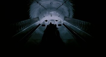 Movie still from “28 Weeks Later” (2007), directed by Juan Carlos Fresnadillo – People are sitting on an escalator in a dark tunnel; Extreme Wide shot, Overhead angle