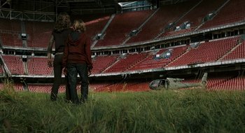Movie still from “28 Weeks Later” (2007), directed by Juan Carlos Fresnadillo – Two people are standing in a field in front of an empty stadium; Extreme Wide shot, High angle