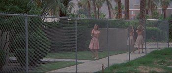 Movie still from “3 Women” (1977), directed by Robert Altman – A woman in a pink dress is standing in front of a fence; Wide shot, Low angle