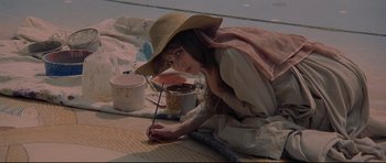 Movie still from “3 Women” (1977), directed by Robert Altman – A woman in a straw hat is painting on the ground; Medium shot, High angle