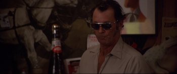 Movie still from “3 Women” (1977), directed by Robert Altman – A man wearing sunglasses is sitting in front of a bottle of beer; Close Up shot, Low angle