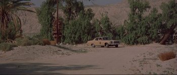 Movie still from “3 Women” (1977), directed by Robert Altman – A couple of cars parked on top of a dirt field; Extreme Wide shot, High angle