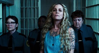 Movie still from “3 from Hell” (2019), directed by Rob Zombie – A woman with long blonde hair standing in front of a group of men; Close Up shot, Over the shoulder angle