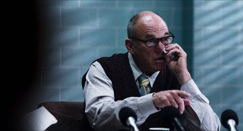 Movie still from “3 from Hell” (2019), directed by Rob Zombie – An older man talking on a cell phone while sitting in front of microphones; Close Up shot, Over the shoulder angle