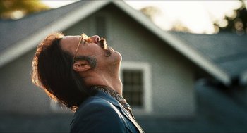 Movie still from “3 from Hell” (2019), directed by Rob Zombie – A man with long hair and a beard standing in front of a house; Close Up shot, Low angle