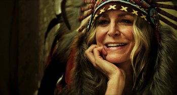 Movie still from “3 from Hell” (2019), directed by Rob Zombie – A woman in a native american headdress smiling for the camera; Close Up shot, Low angle