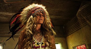 Movie still from “3 from Hell” (2019), directed by Rob Zombie – A woman in a native american headdress and tattoos; Close Up shot, Low angle