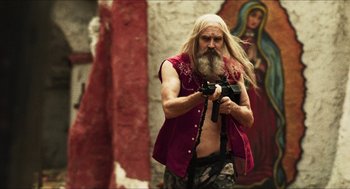 Movie still from “3 from Hell” (2019), directed by Rob Zombie – A man with long white hair holding a camera in his hand; Medium shot, Low angle
