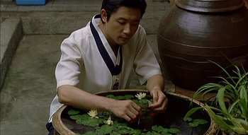 A man sitting in front of a bowl of water with water lilies