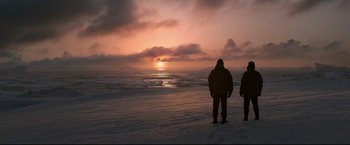 Two people standing on the beach watching the sun go down