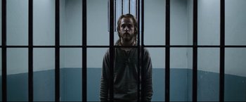 Movie still from “30 Days of Night” (2007), directed by David Slade – A man standing behind bars in front of a window; Medium shot, Low angle