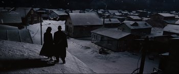 Movie still from “30 Days of Night” (2007), directed by David Slade – Two people standing in the snow looking at houses in the distance; Extreme Wide shot, High angle