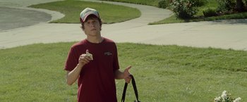 Movie still from “30 Minutes or Less” (2011), directed by Ruben Fleischer – A young man standing in a park holding a sandwich; Medium shot, Over the shoulder angle