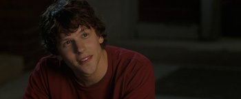 Movie still from “30 Minutes or Less” (2011), directed by Ruben Fleischer – A young man in a red shirt smiling for the camera; Close Up shot, Over the shoulder angle
