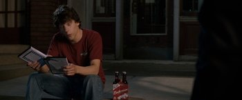 Movie still from “30 Minutes or Less” (2011), directed by Ruben Fleischer – A man sitting on the ground next to a six - pack of beer; Medium shot, High angle