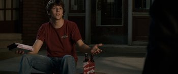 Movie still from “30 Minutes or Less” (2011), directed by Ruben Fleischer – A man sitting on the ground holding a beer bottle; Medium shot, High angle