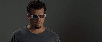 Movie still from “30 Minutes or Less” (2011), directed by Ruben Fleischer – A man wearing 3 - d glasses while standing in front of a gray wall; Close Up shot, Low angle