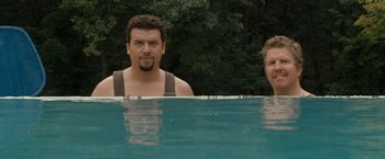 Movie still from “30 Minutes or Less” (2011), directed by Ruben Fleischer – Two men standing in a swimming pool with trees in the background; Medium shot, Over the shoulder angle