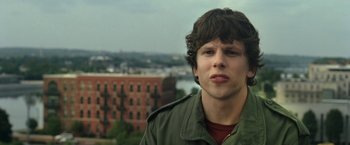 Movie still from “30 Minutes or Less” (2011), directed by Ruben Fleischer – A man in a green jacket is standing in front of a building; Close Up shot, Over the shoulder angle