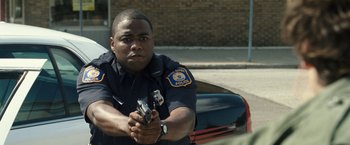 Movie still from “30 Minutes or Less” (2011), directed by Ruben Fleischer – A police officer is holding a gun in his hand; Medium shot, Low angle