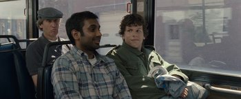 Movie still from “30 Minutes or Less” (2011), directed by Ruben Fleischer – Two men are sitting on a bus and smiling; Medium shot, Over the shoulder angle