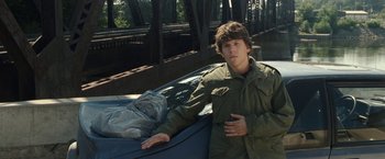 Movie still from “30 Minutes or Less” (2011), directed by Ruben Fleischer – A young man leaning on the hood of a car; Medium shot, Over the shoulder angle