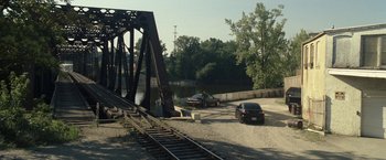 Movie still from “30 Minutes or Less” (2011), directed by Ruben Fleischer – A couple of cars parked on top of train tracks near a bridge; Extreme Wide shot, High angle