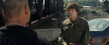 Movie still from “30 Minutes or Less” (2011), directed by Ruben Fleischer – A young man standing next to a bridge; Medium shot, Over the shoulder angle