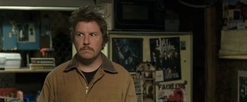 Movie still from “30 Minutes or Less” (2011), directed by Ruben Fleischer – A man standing in front of a bunch of pictures; Close Up shot, Over the shoulder angle