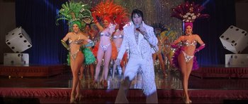 Movie still from “3000 Miles to Graceland” (2001), directed by Demian Lichtenstein – A man in a white suit is on a stage; Wide shot, Over the shoulder angle