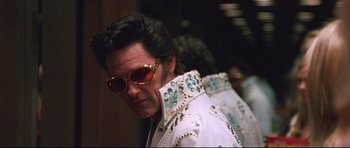 Movie still from “3000 Miles to Graceland” (2001), directed by Demian Lichtenstein – A person wearing sunglasses and a white jacket; Medium shot, Low angle